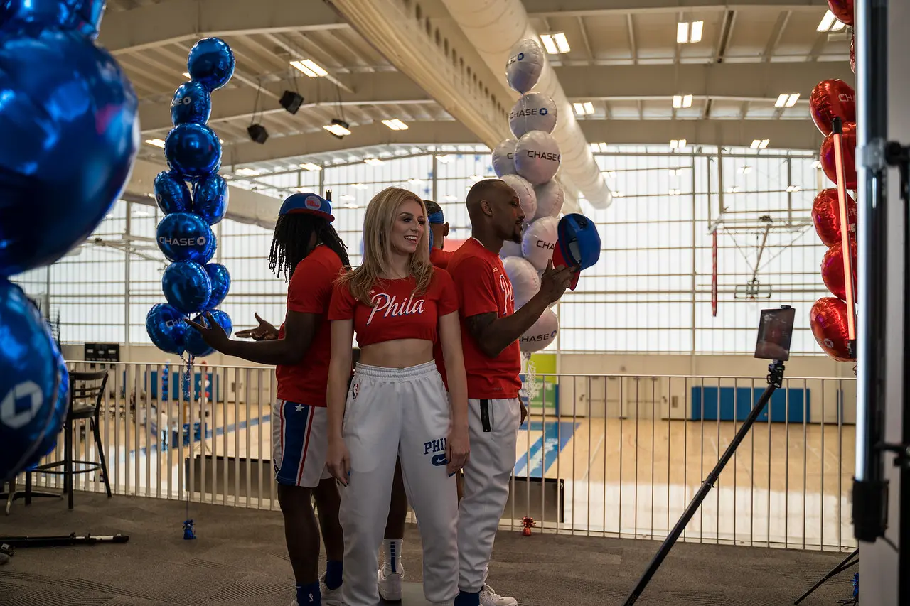 Three men and a woman, wearing Phila apparel, standing with their backs to each other, surrounded by balloons